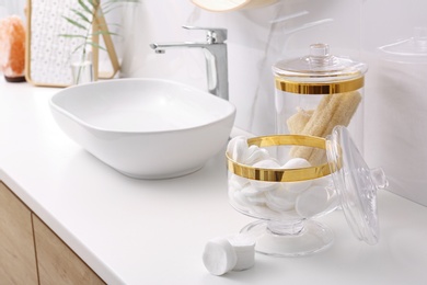 Glass jars with cotton pads and loofahs on table in bathroom