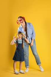 Photo of Happy woman and daughter with funny glasses on color background