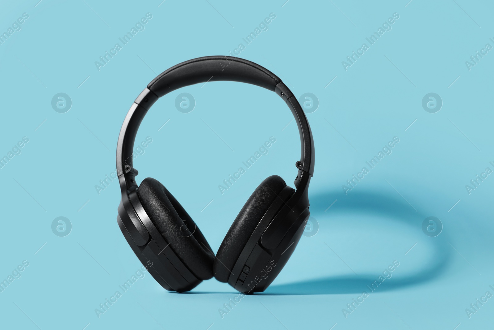 Photo of Modern wireless headphones on light blue background, space for text