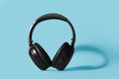 Modern wireless headphones on light blue background, space for text