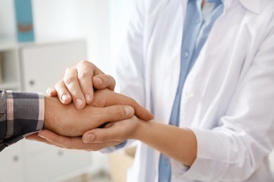 Photo of Female doctor comforting man on blurred background, closeup of hands. Help and support concept