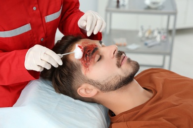 Photo of Nurse cleaning young man's head injury in clinic. First aid