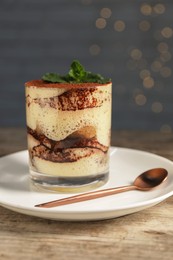 Photo of Tasty tiramisu and mint in glass on wooden table, closeup