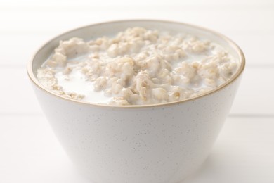 Photo of Tasty boiled oatmeal in bowl on white table, closeup