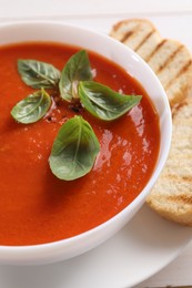 Delicious tomato cream soup in bowl with pieces of grilled bread on white table, closeup