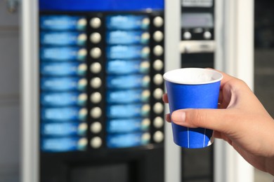 Image of Woman with paper cup of beverage near coffee vending machine, closeup