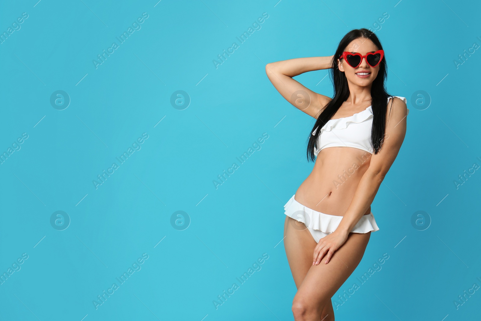 Photo of Beautiful young woman in white bikini with sunglasses on light blue background. Space for text
