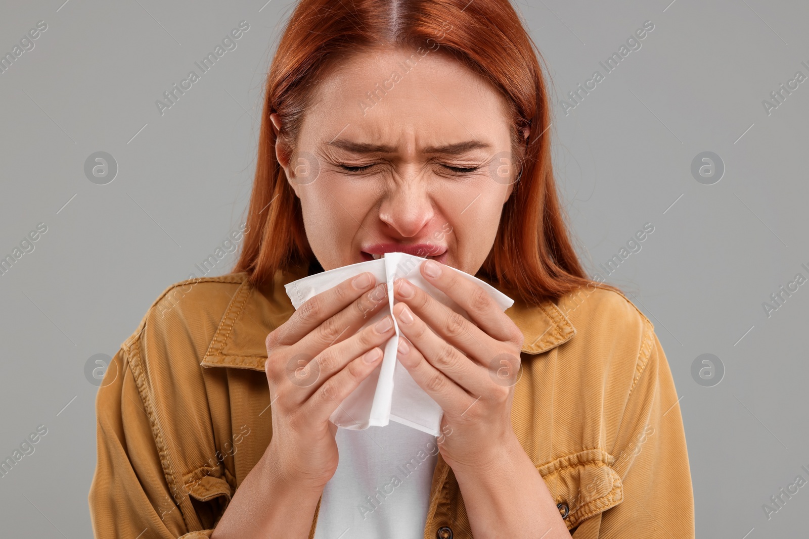 Photo of Suffering from allergy. Young woman with tissue sneezing on grey background