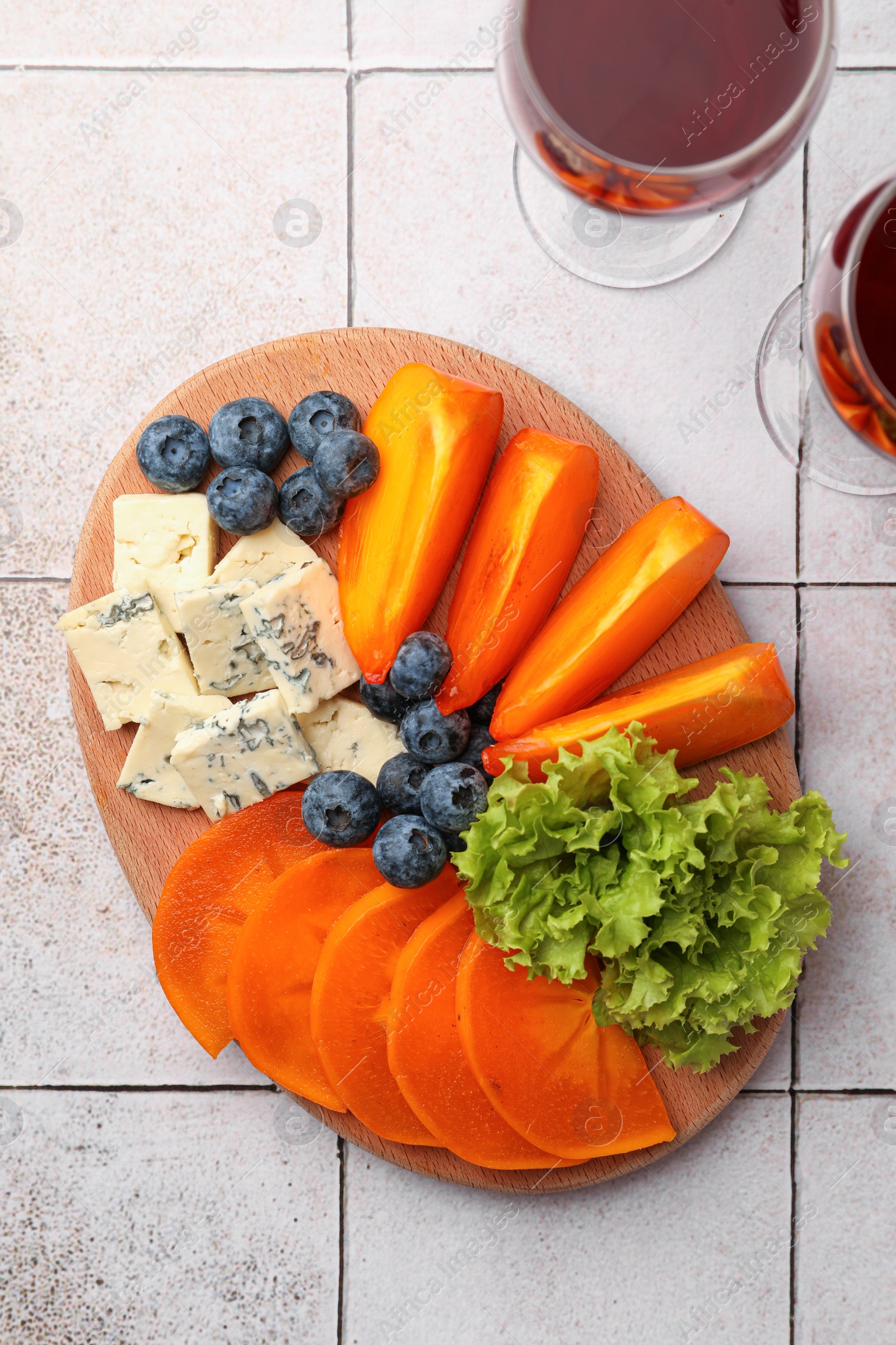 Photo of Delicious persimmon, blue cheese and blueberries on tiled surface, flat lay