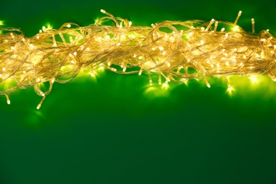 Glowing Christmas lights on green background, top view. Space for text