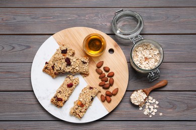 Photo of Tasty granola bars and ingredients on grey wooden table, flat lay