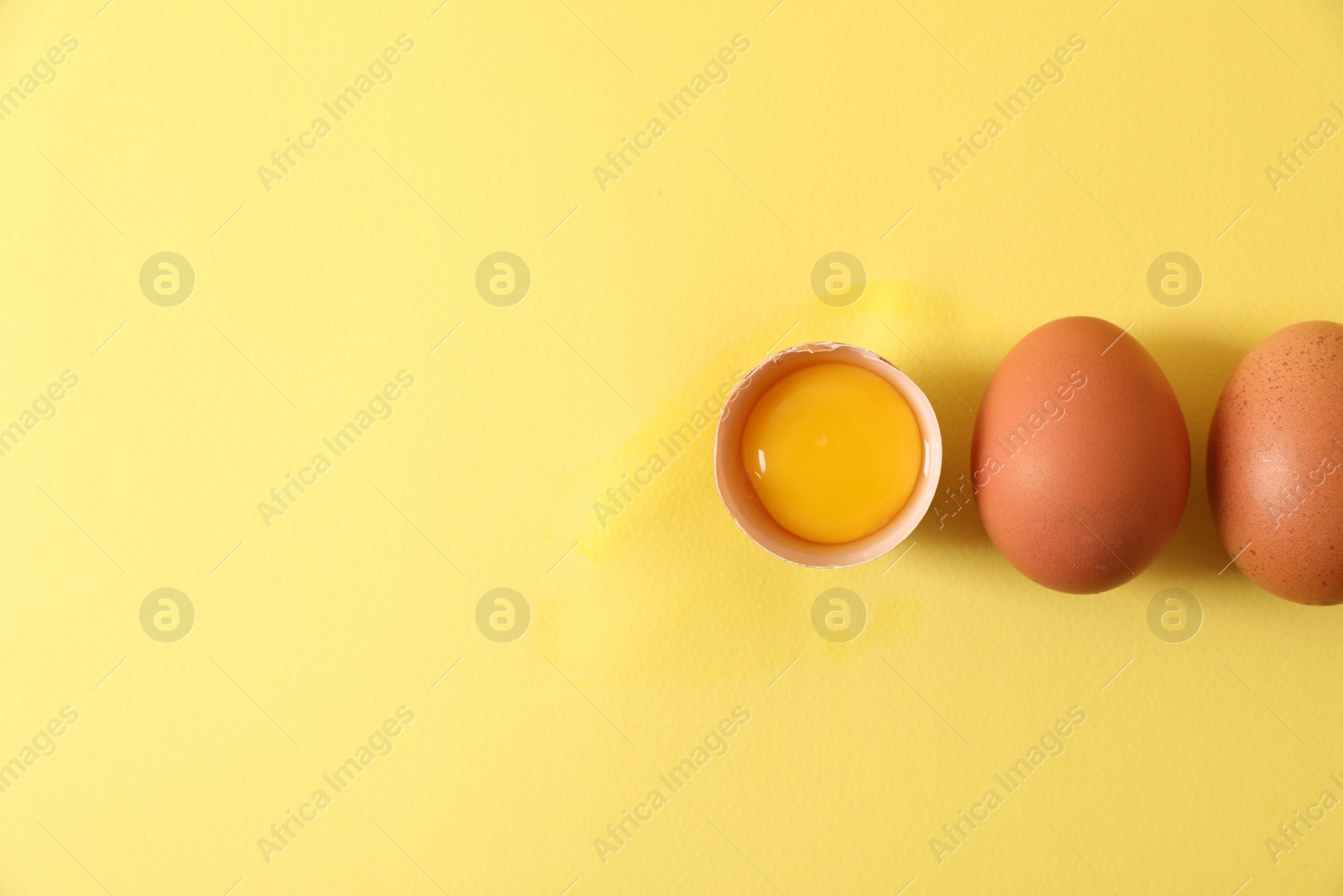 Photo of Cracked and whole chicken eggs on yellow background, flat lay. Space for text