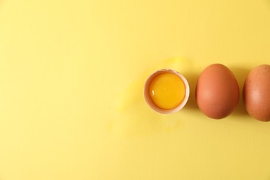 Cracked and whole chicken eggs on yellow background, flat lay. Space for text