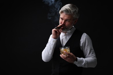 Bearded man with glass of whiskey smoking cigar against black background. Space for text