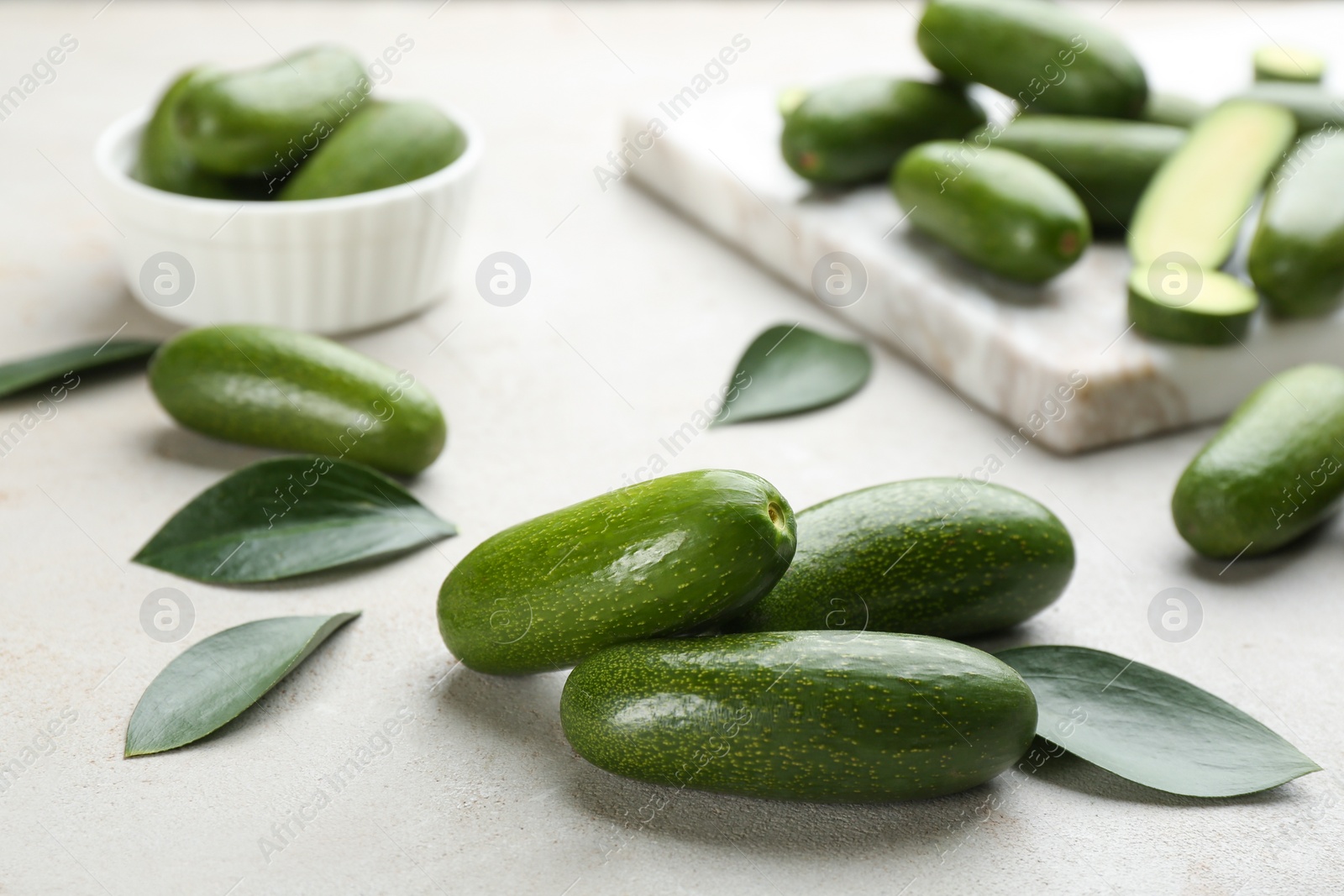 Photo of Whole seedless avocados with green leaves on light grey table