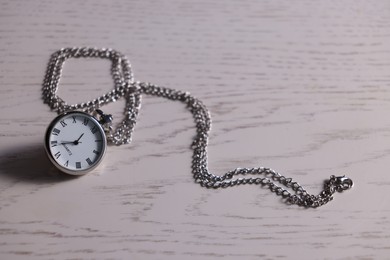 Photo of Silver pocket clock with chain on light wooden table, closeup