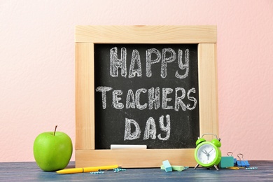 Photo of Little blackboard with inscription HAPPY TEACHER'S DAY, alarm clock and apple on table