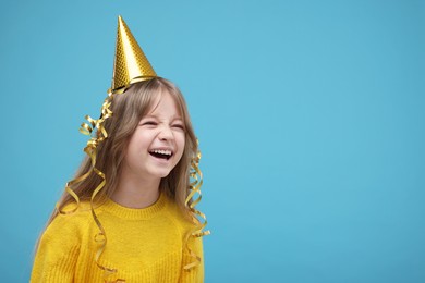 Photo of Cute little girl in party hat laughing on light blue background. Space for text