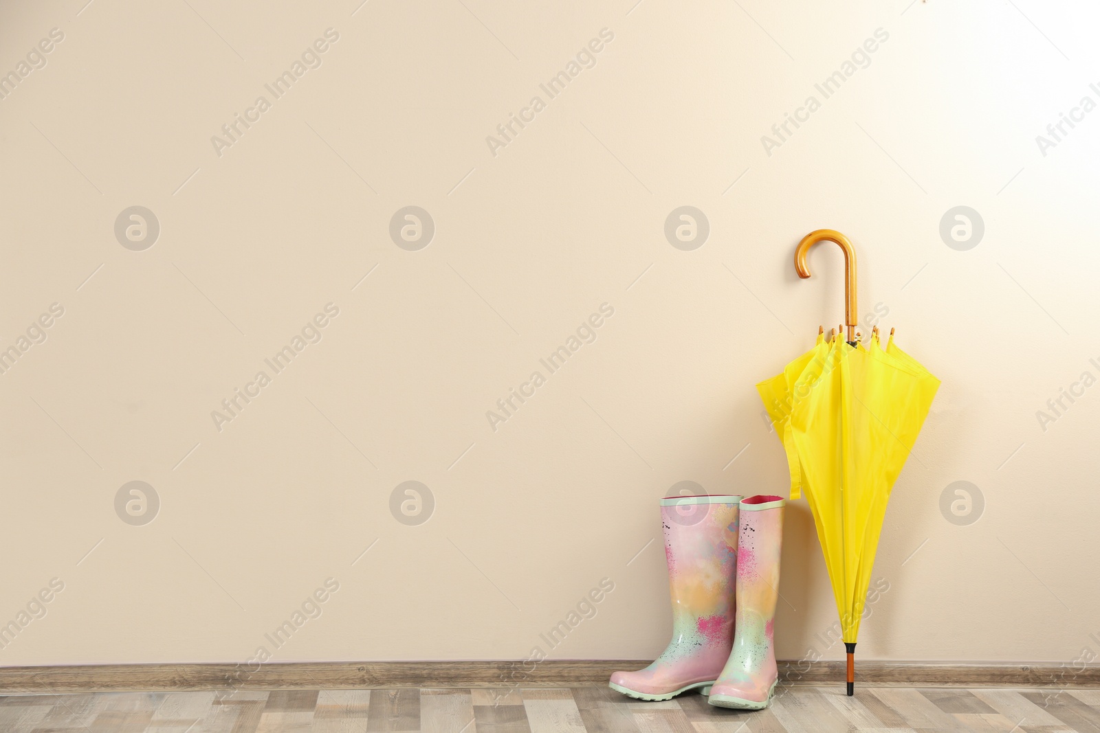 Photo of Beautiful yellow umbrella and rubber boots near beige wall. Space for text