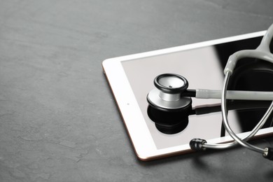 Modern tablet and stethoscope on black table, closeup. Space for text