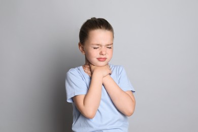 Photo of Little girl suffering from sore throat on grey background