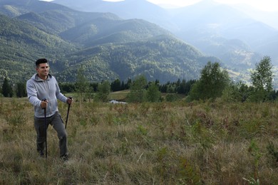 Photo of Tourist with trekking poles hiking through mountains, space for text