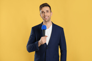 Young male journalist with microphone on yellow background