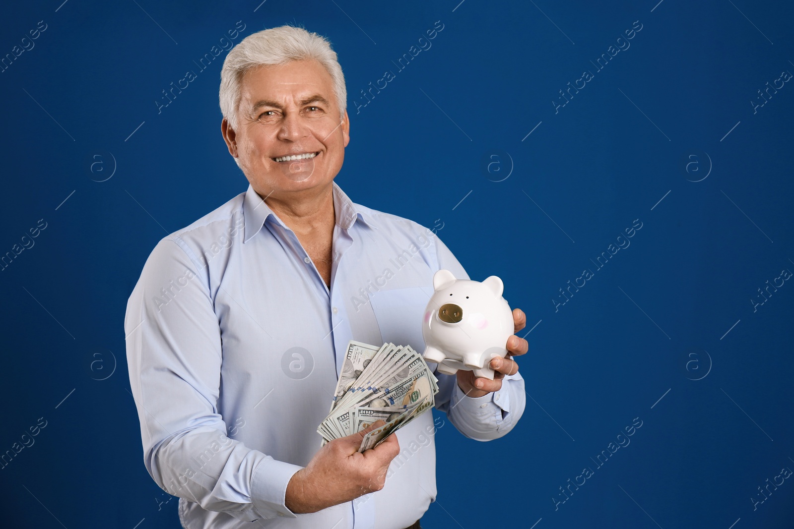 Photo of Happy senior man with cash money and piggybank on blue background