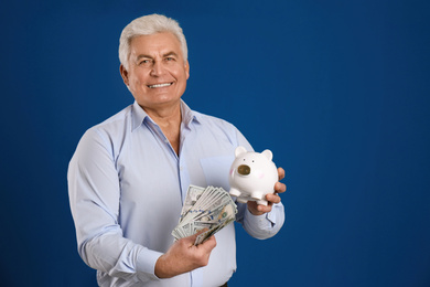 Photo of Happy senior man with cash money and piggybank on blue background