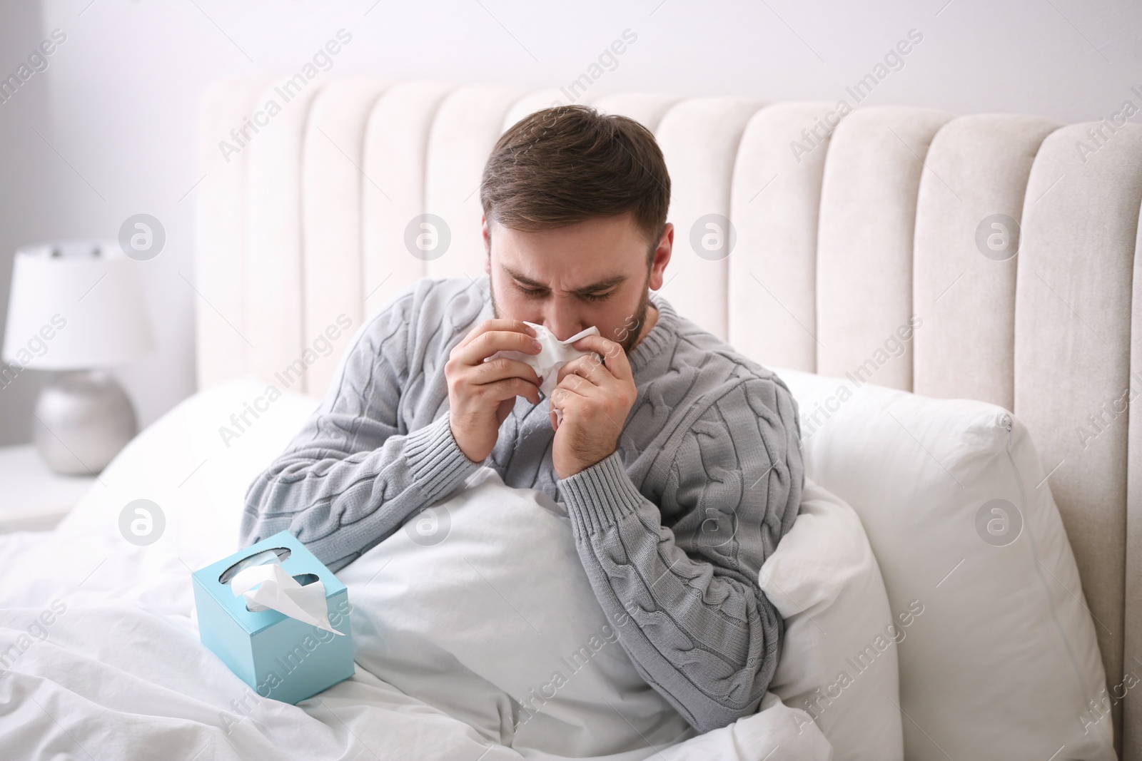 Photo of Young man suffering from runny nose in bed indoors