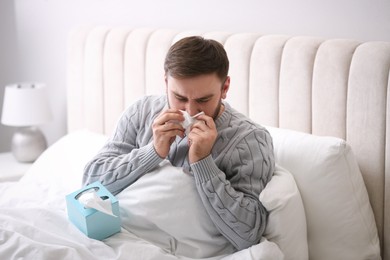 Young man suffering from runny nose in bed indoors