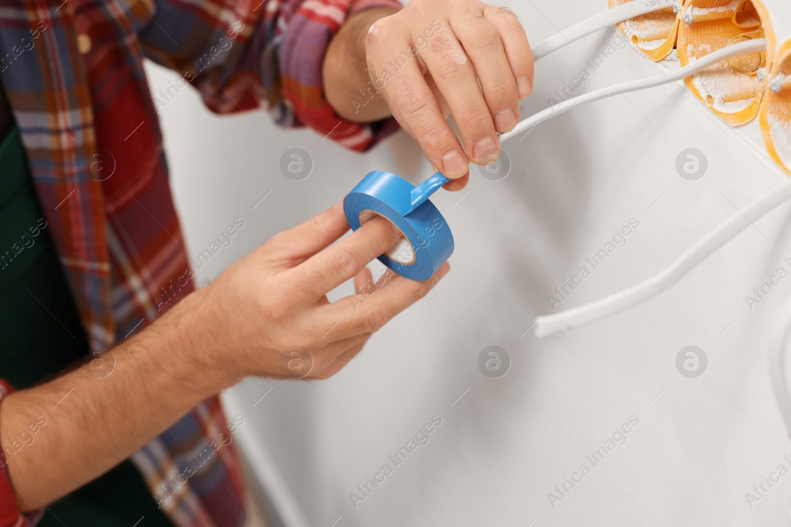 Photo of Electrician fixing wires with insulating tape indoors, closeup