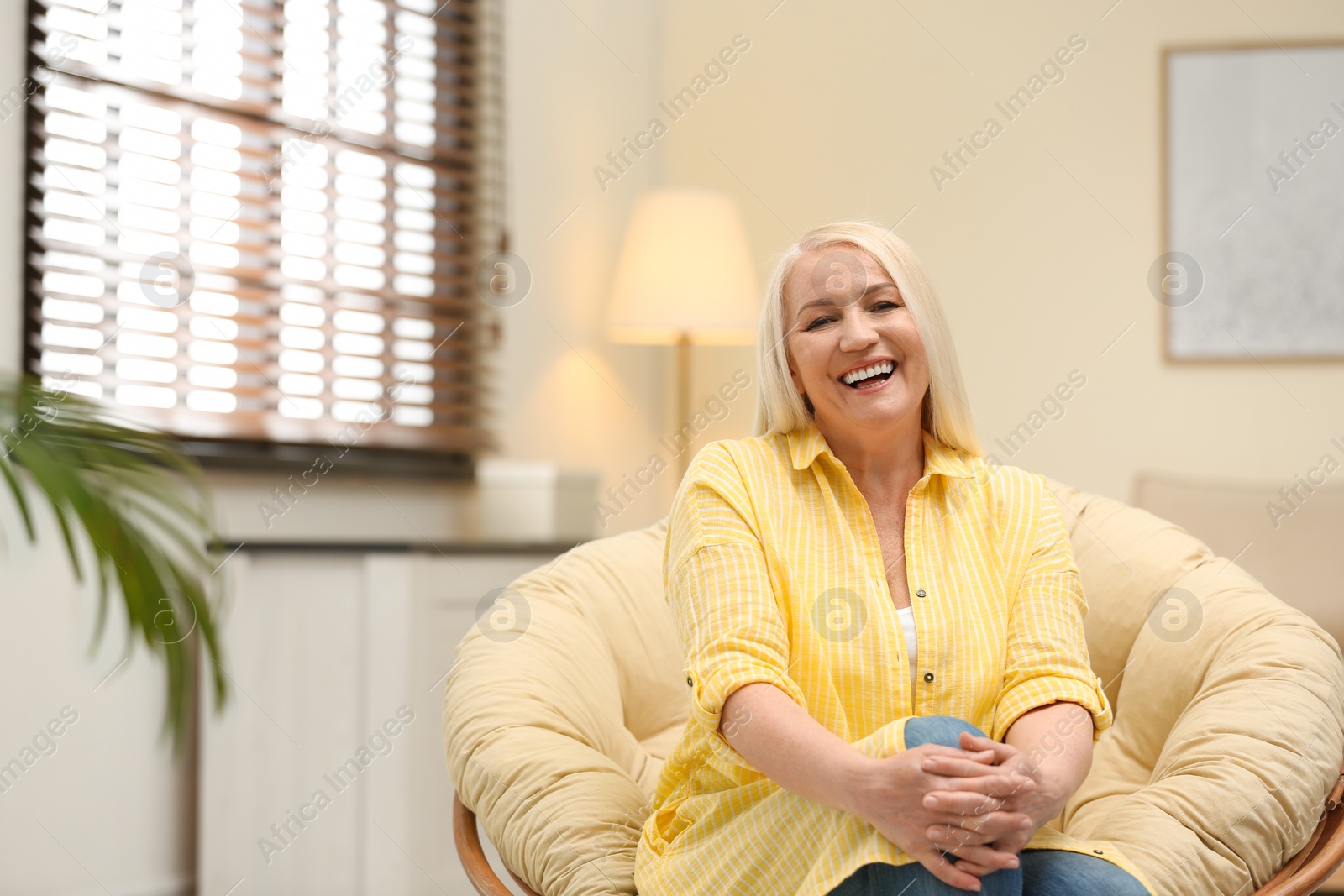 Photo of Portrait of happy mature woman sitting in papasan chair at home