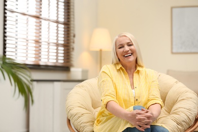 Portrait of happy mature woman sitting in papasan chair at home