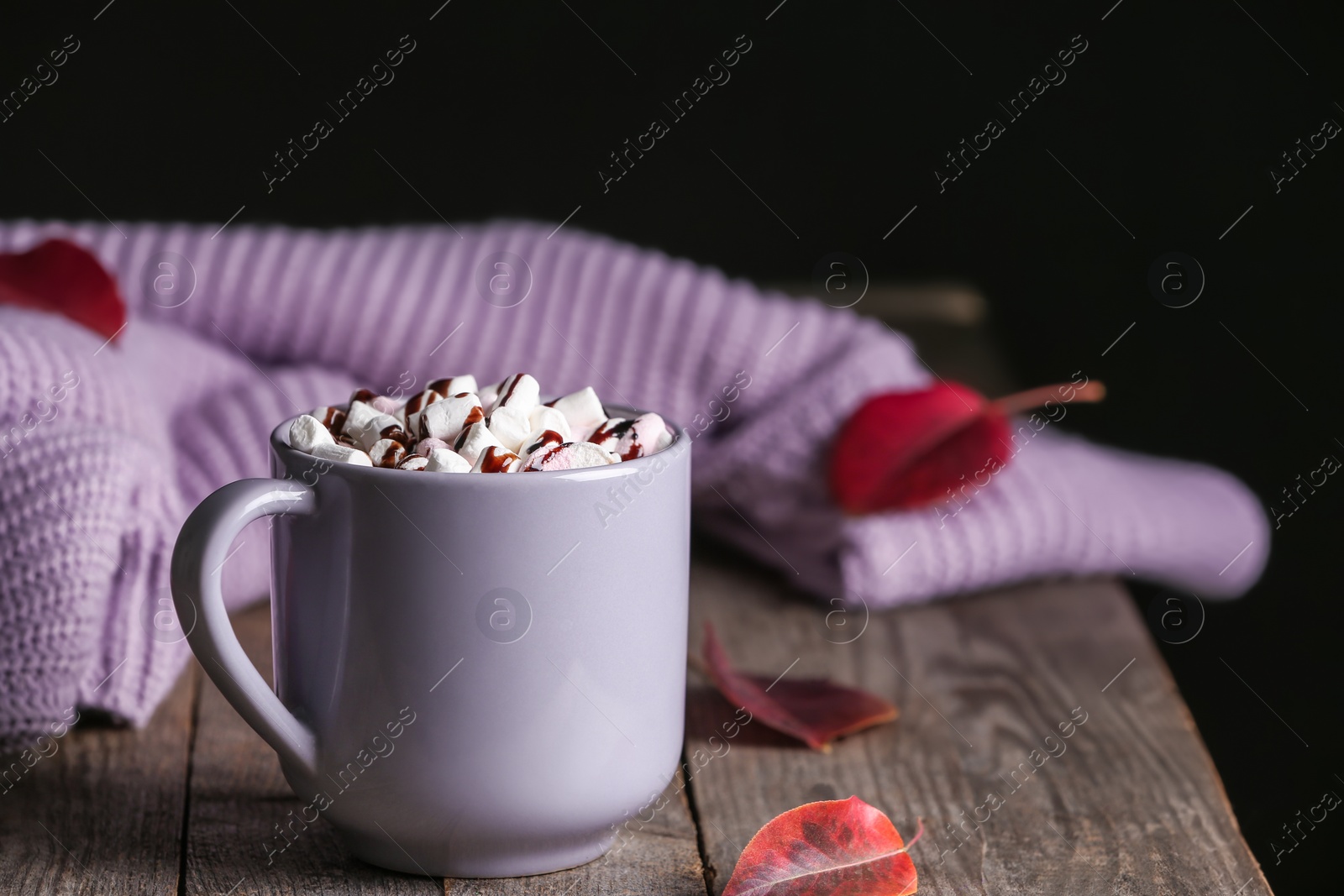 Photo of Cup of hot cozy drink, autumn leaves and clothing on wooden table. Space for text