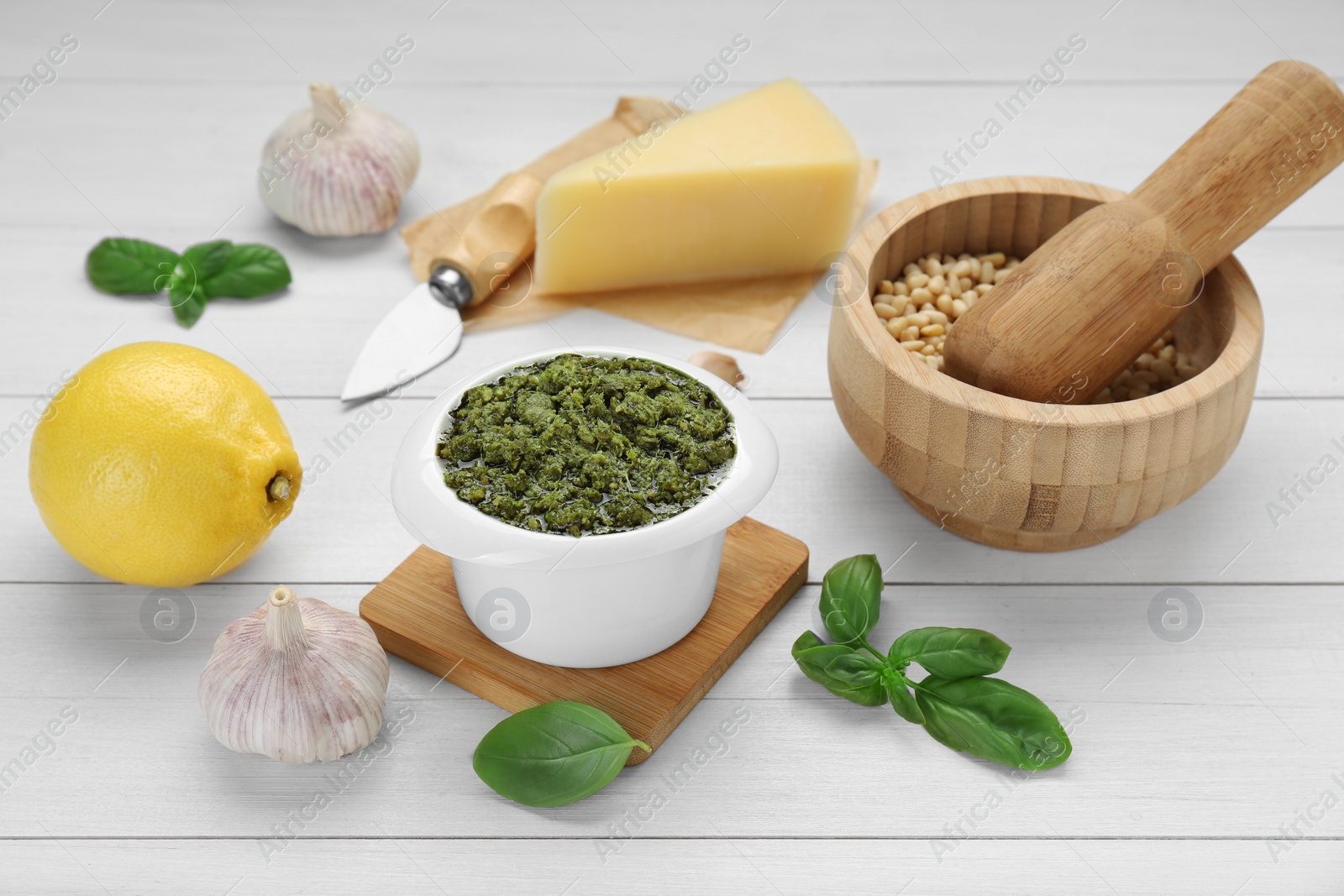 Photo of Delicious pesto sauce in bowl and ingredients on white wooden table