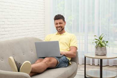 Happy man using laptop on sofa at home. Internet shopping