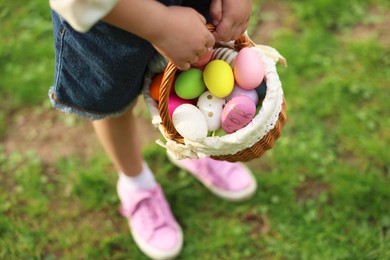 Photo of Easter celebration. Little girl holding basket with painted eggs outdoors, closeup