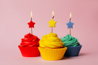 Delicious birthday cupcakes with burning candles on pink background