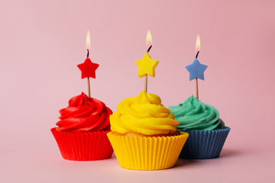 Photo of Delicious birthday cupcakes with burning candles on pink background