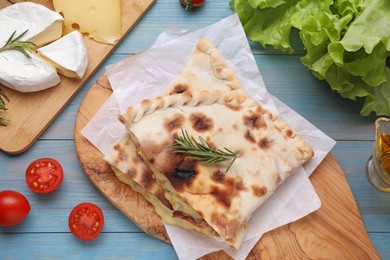 Photo of Tasty pizza calzones with cheese, rosemary and different products on light blue wooden table, flat lay