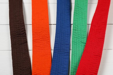 Photo of Colorful karate belts on wooden background, flat lay