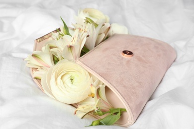 Photo of Stylish clutch with spring flowers on crumpled sheet