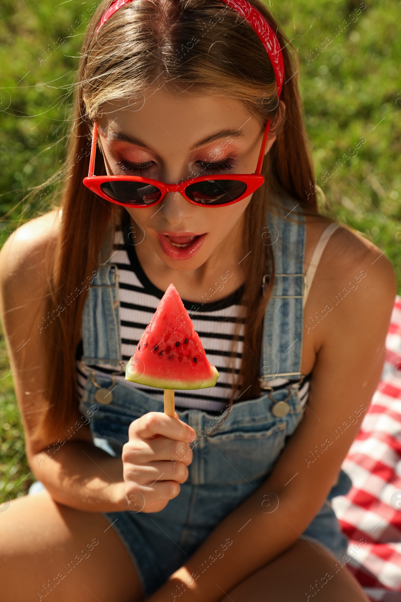 Photo of Beautiful girl with piece of watermelon on picnic blanket outdoors