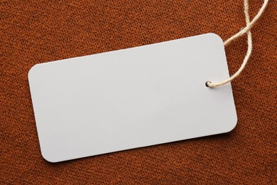 Photo of Cardboard tag with space for text on brown fabric, top view