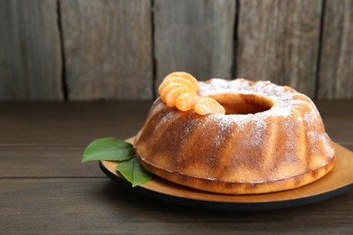 Homemade yogurt cake with tangerines, powdered sugar and green leaves on wooden table. Space for text