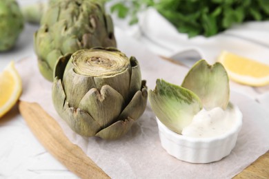 Photo of Delicious cooked artichoke with tasty sauce served on table, closeup