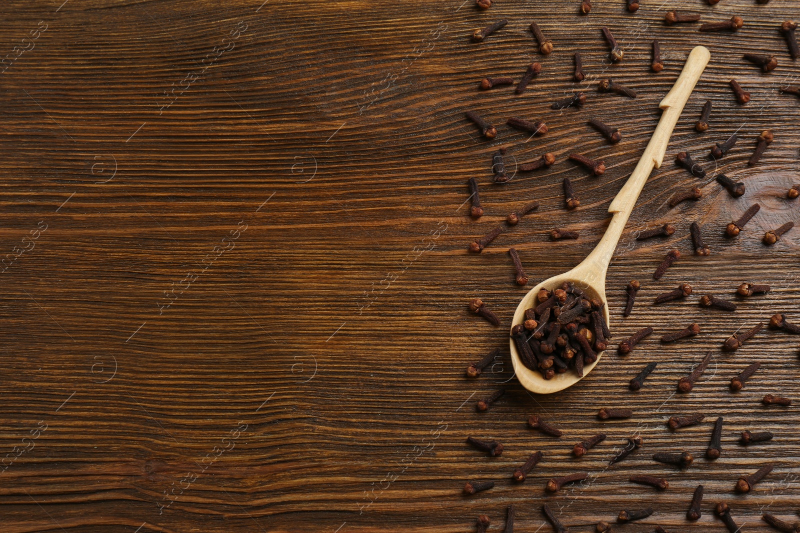 Photo of Aromatic dry cloves and spoon on wooden table, flat lay. Space for text