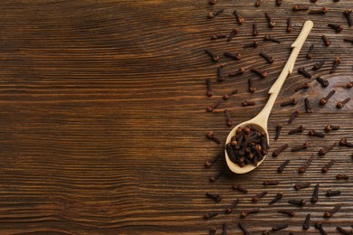 Aromatic dry cloves and spoon on wooden table, flat lay. Space for text