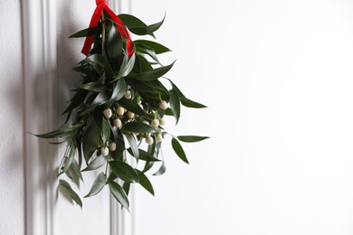 Photo of Mistletoe bunch with red ribbon hanging on light background, space for text. Traditional Christmas decoration